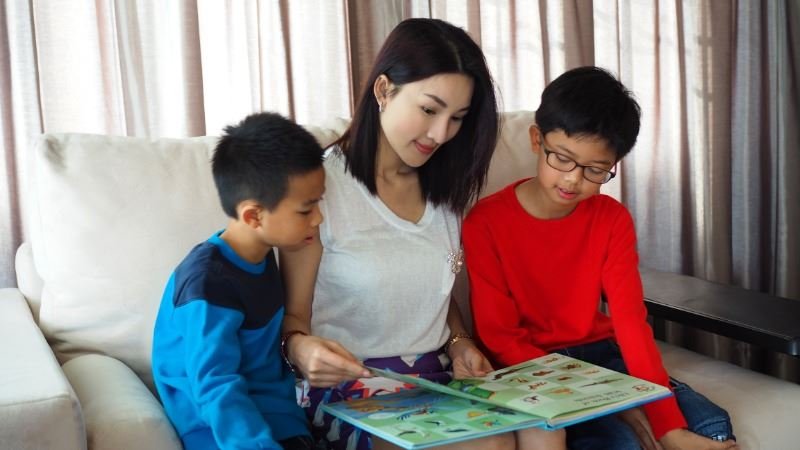 一位母親和她的兩個兒子一起坐在沙發上讀一本英文故事書。透過故事學習英語。