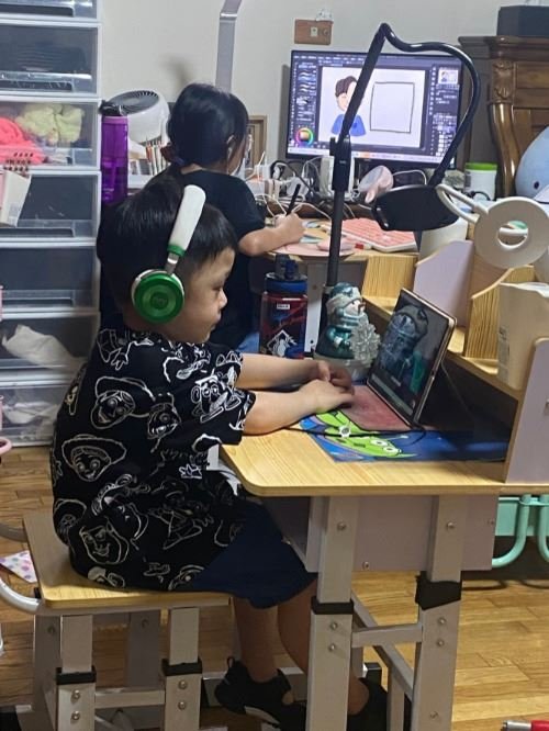 兩個孩子使用帶耳機的書桌和電腦進行線上學習。