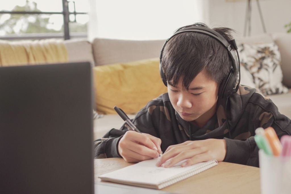 男孩戴著耳機,專注於線上學習,做筆記。為孩子選擇合適的線上英語課程。