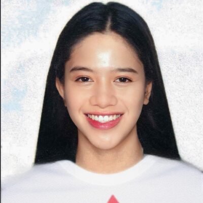 一位面帶微笑的年輕女子的肖像，她有著長長的黑髮，穿著白襯衫。