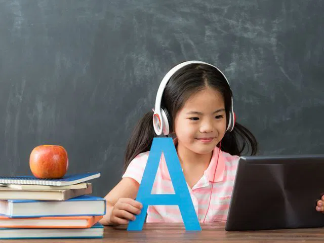 女孩戴著耳機在網路上學習,手裡拿著字母 A。