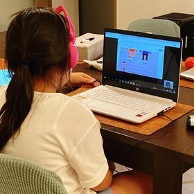 學生戴著粉紅色耳機使用筆記型電腦上網課。