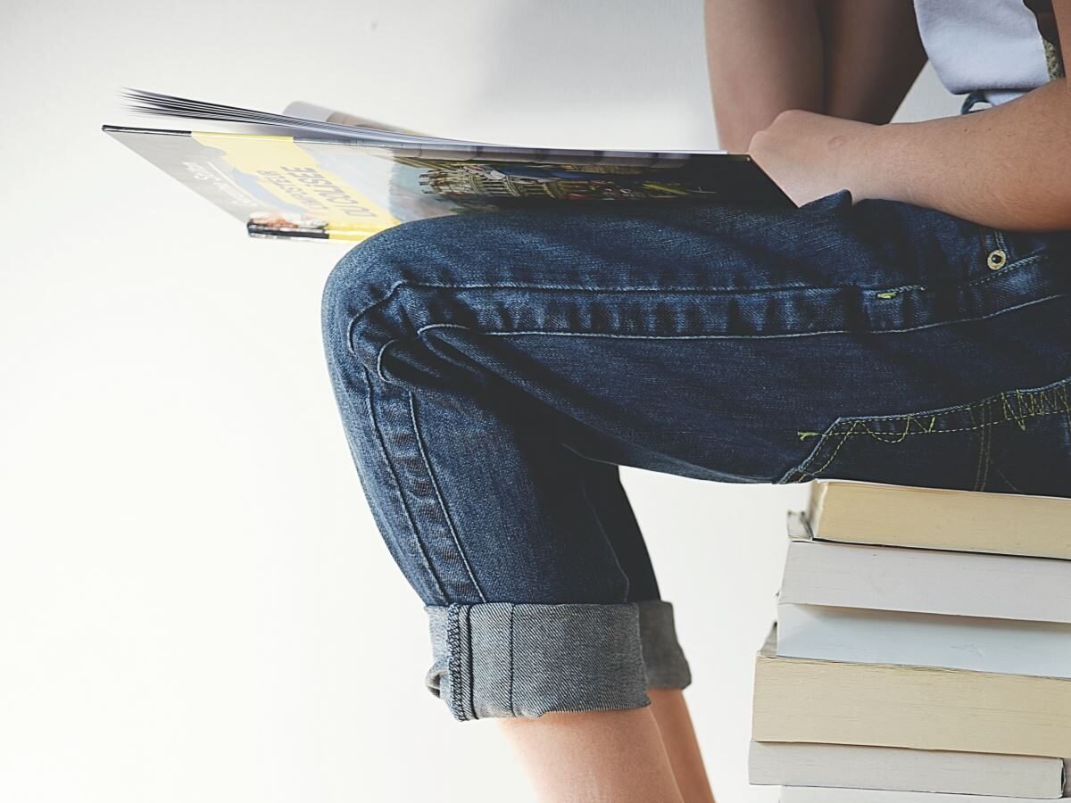 穿著牛仔褲的人坐在一堆書上閱讀旅遊指南。