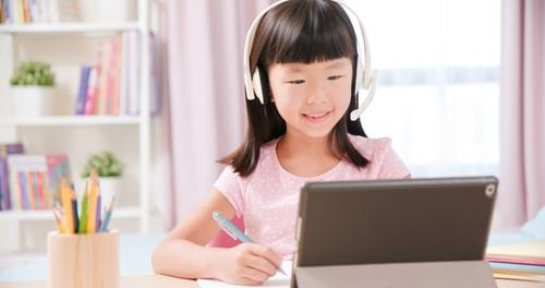 小女孩戴著耳機，使用平板電腦在線上學習英語。